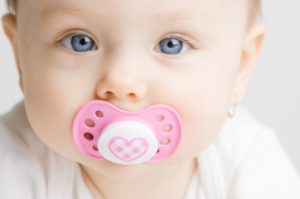Frontal view of a cute baby girl with a soother in her mouth