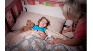 child being tucked into bed by a woman