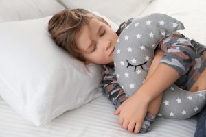 fears - a child laying on a white pillow. Child has brown hair and his hugging a grey moon shaped pillow.