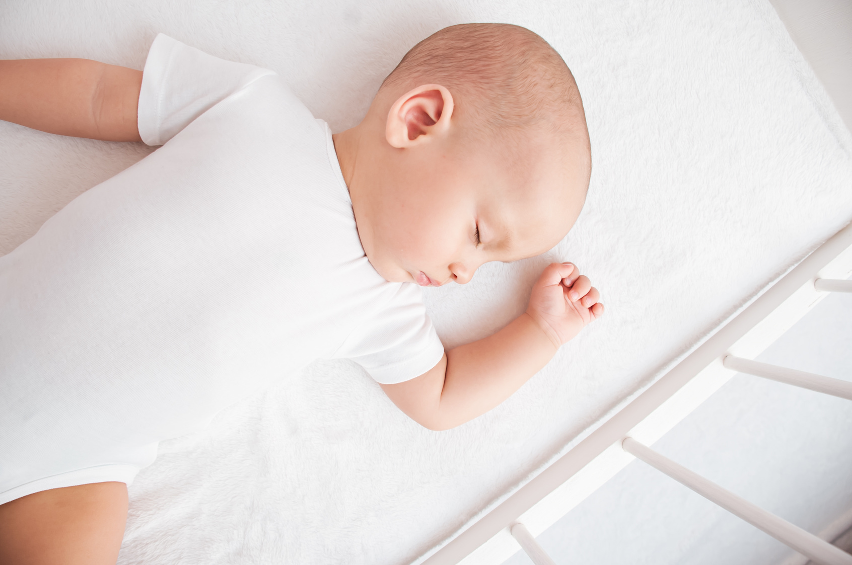 know - baby sleping on back in a white onesie in a white crib on a white sheet