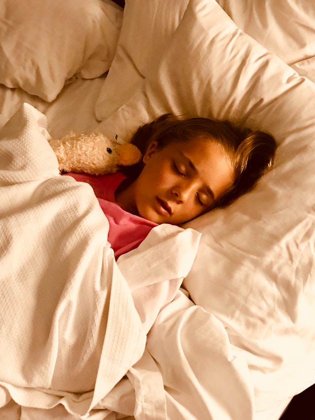 sleep for school aged kids - photo of a person laying in a bed (looks to be 5-8 years old) with a pink shirt and long brown hair and sleeping