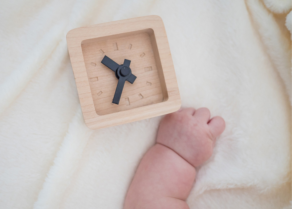 early - photo of a baby hand next to a wooden clock