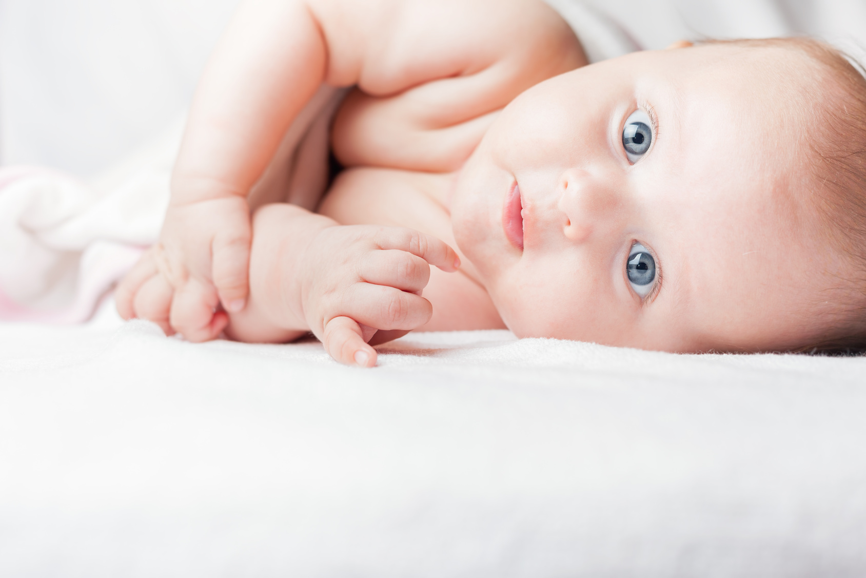 naps - a close up of a baby on their side looking at the camera - laying on a white blanket