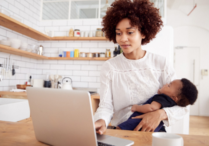 Mother holding newborn baby while browsing laptop