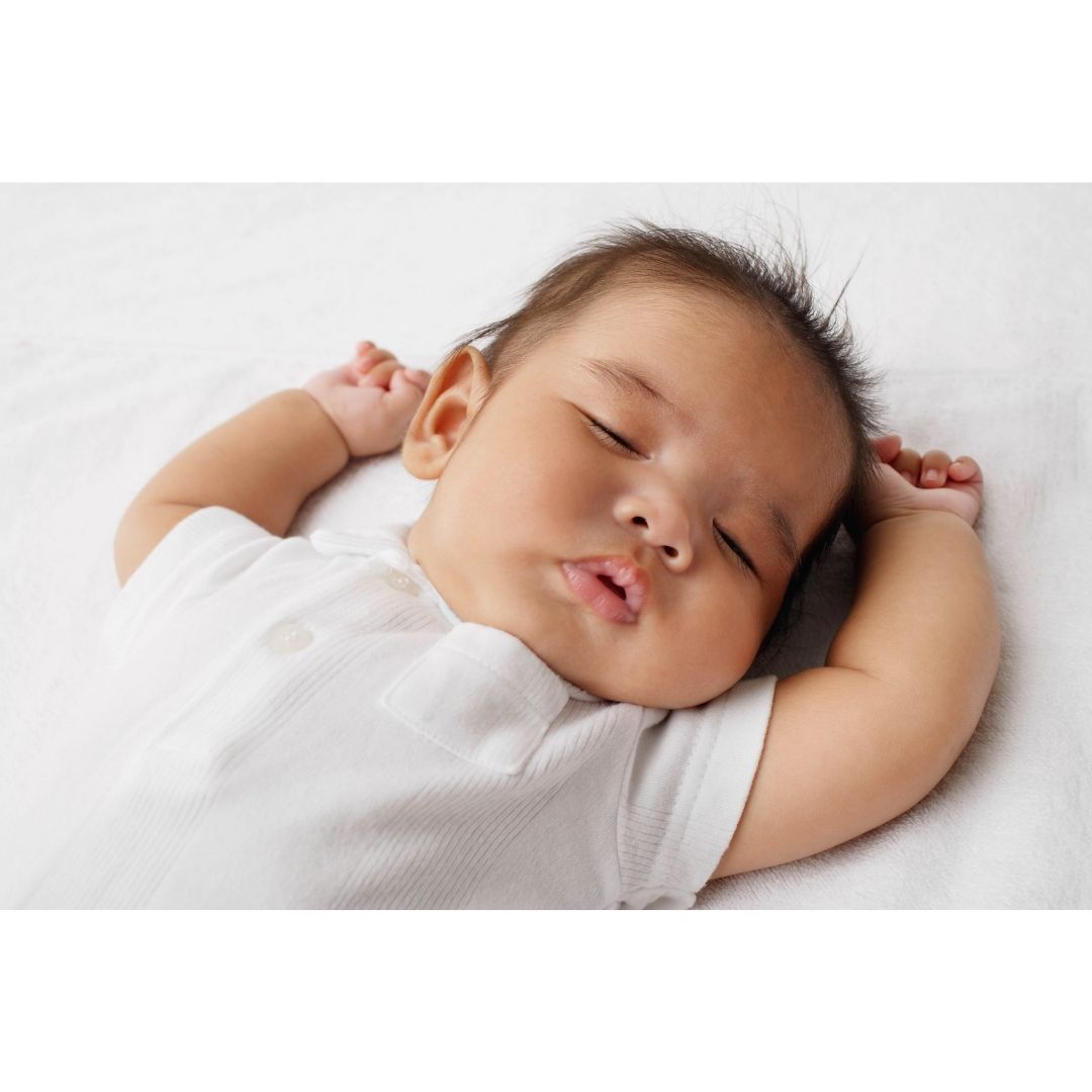 nap - an image of a baby with dark hair, waring a white onesie laying with their arms above head on a white sheet