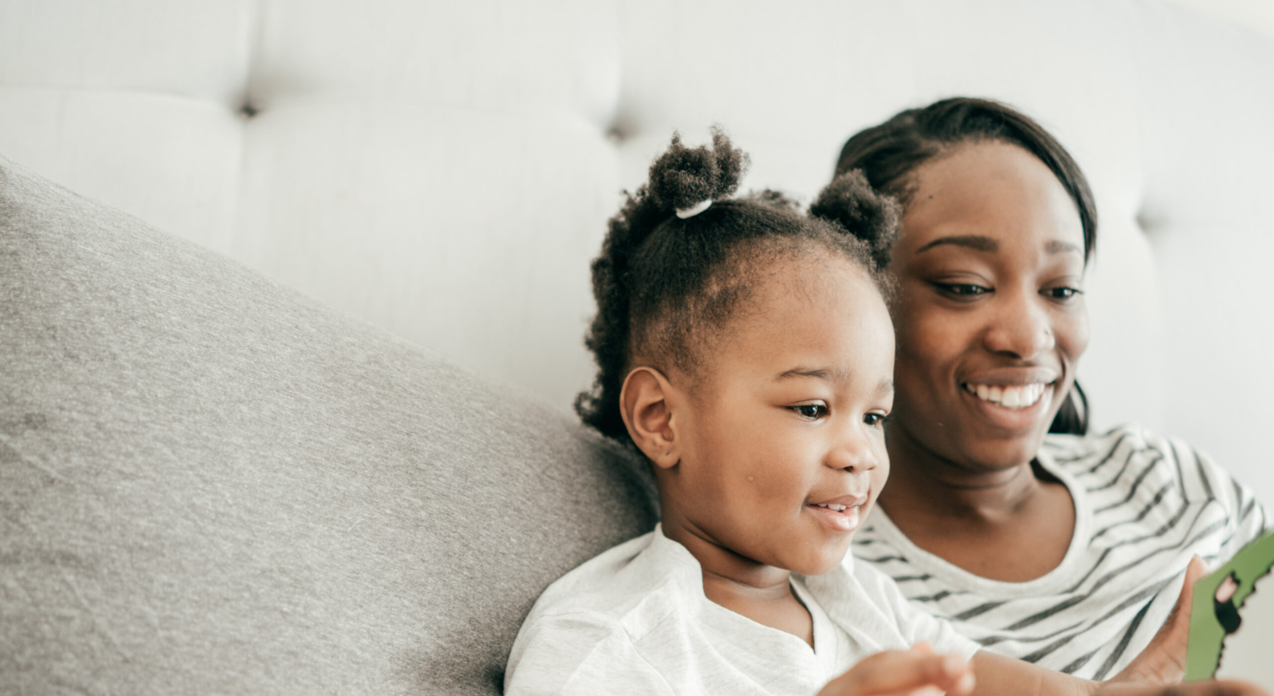 Bedtime tips: Mom and daughter reading a book on a couch - sharing tips on what to do when your child prefers one parent over the other.