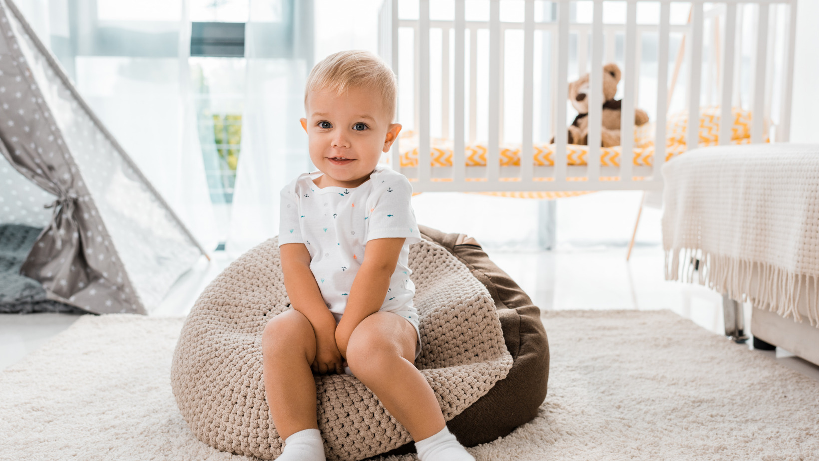 New bedroom - baby in white t-shirt sitting on a grey poof stool