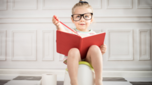 Potty training: child sitting on a potty with a red book and big glasses