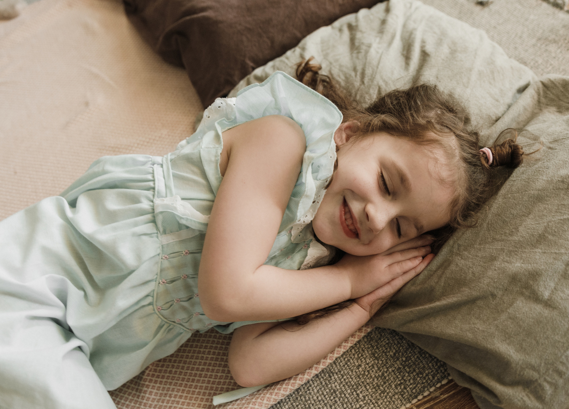 Smiling female child laying down in bed with head resting on a pillow