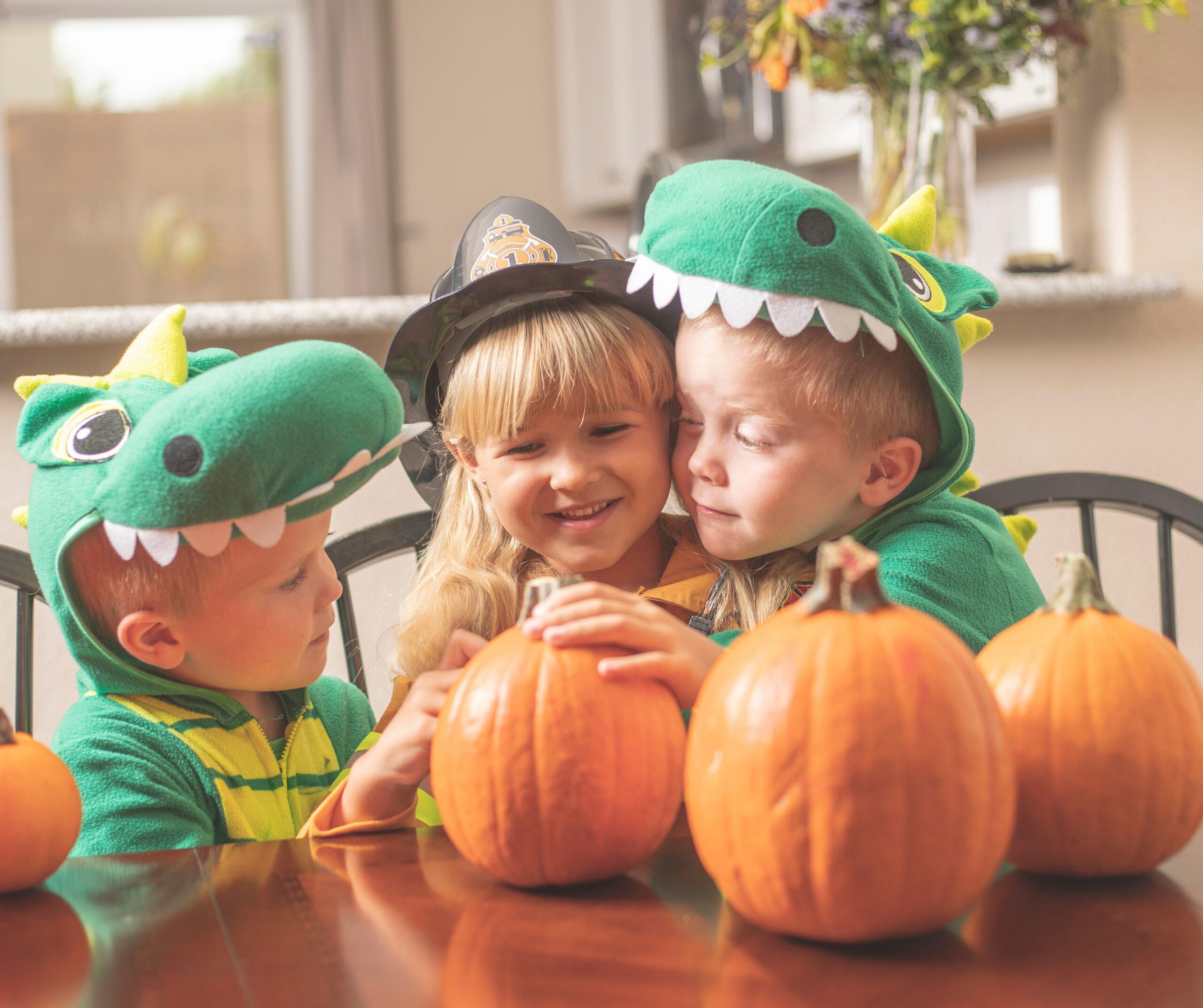 Halloween - kids in dinosaur costumes sitting at a table in the kitchen with pumpkins