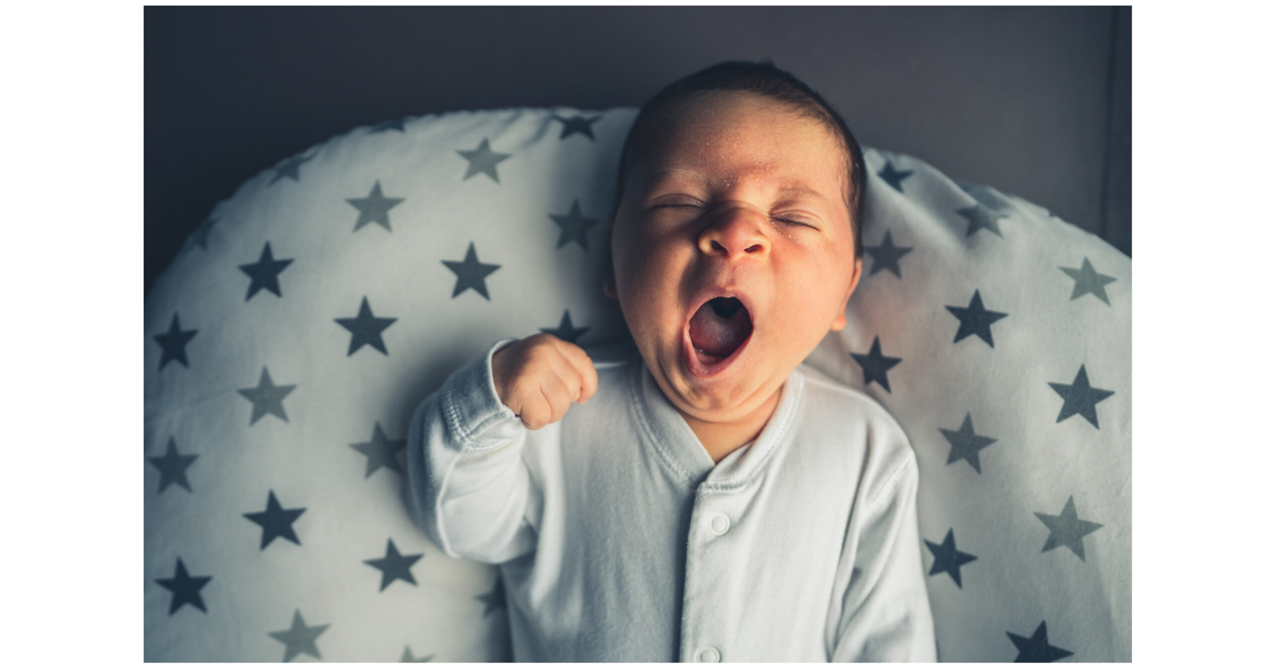 unsafe sleep setuo - baby with a huge yawn laying on a star patterned nursing pillow