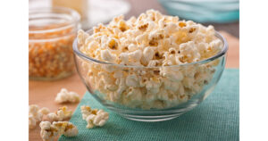Eat: bowl of popcorn on a teal mat with unpopped kernals in a glass jar behind the bowl
