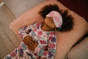 Tips to beat sleeping in the heat! Child lying in bed with eye mask as viewed from above.