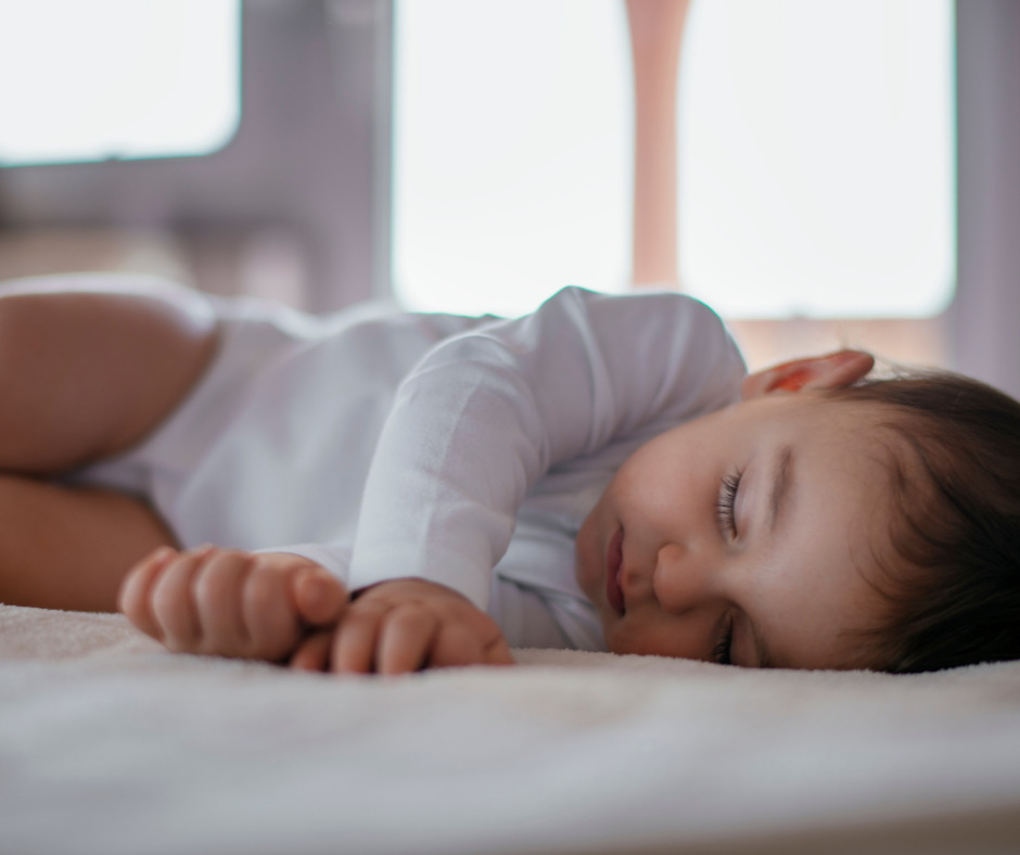 Baby sleeping in a white long sleeve onesie on a Montessori Bed