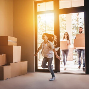 It's Moving Day! Tips to Make the Transition Easier for Sleep - a room full of boxes with a child running into the room, 2 adults behind holding boxes and a sun flare coming through the window